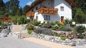 A two-story house with a balcony, surrounded by a garden with various plants and flowers. - Holiday Apartment at the Rose Garden (Fuessen)