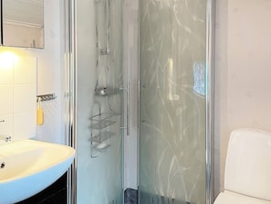 Ein Badezimmer mit Duschkabine aus Glas, Waschbecken in Weiß und Toilette.