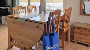 Un comedor con una mesa y sillas de madera, un bolso azul y vistas a árboles a través de amplias ventanas.