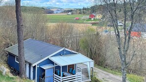 Una cabaña azul con un porche, rodeada de árboles y un campo cubierto de hierba.