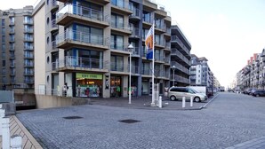 En byggnad med flera våningar, där bottenvåningen inrymmer en barnbutik, en flaggstång med en flagga och ett stenlagt område med pollare.