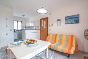 A compact living space with a dining table, a sofa, a kitchen area, and a view of the sea. - Seaside Villa Retreat in Stintino (Stintino)