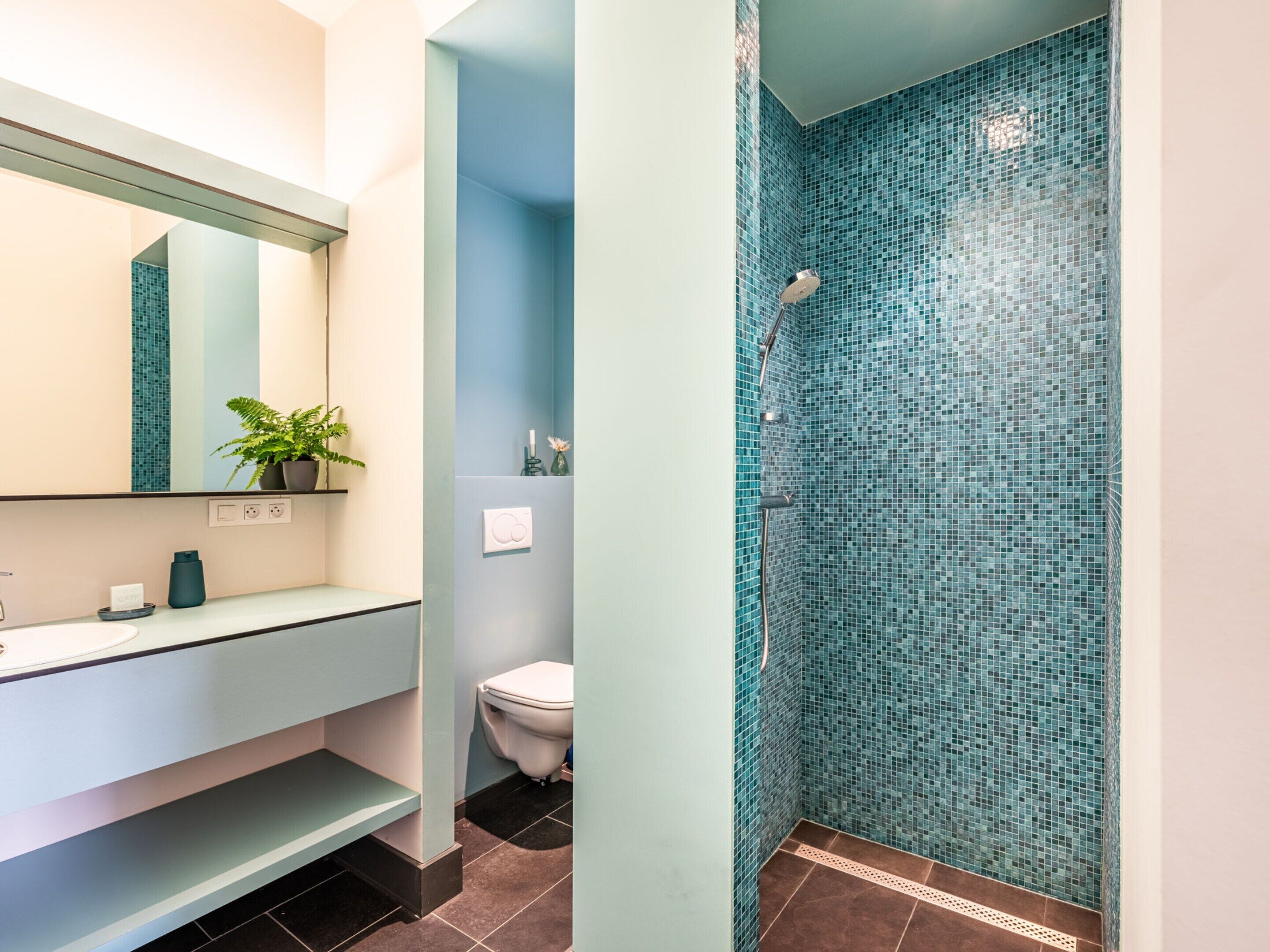 Un baño con lavamanos, espejo y ducha con mosaicos.
