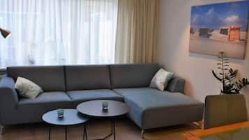 A modern living room with a grey sectional sofa, two round tables, and a framed painting on the wall.
