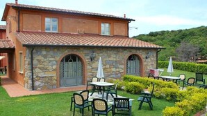 A stone building with a tiled roof, outdoor seating with tables and chairs, and a well-maintained garden. - Spacious Apartment With Bubble Bath (Monteverdi Marittimo)