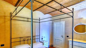 A four-poster bed with a patterned bedspread, a bedside table with a lamp, a white door, and a mirror on the wall. - Spacious Apartment With Bubble Bath (Monteverdi Marittimo)