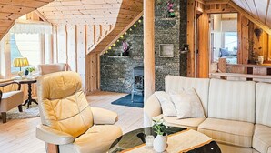 A cozy cabin interior with a wooden ceiling, a stone fireplace, a sofa, and a chair. - 8 Person Holiday Home in Bygstad (Sunnfjord)