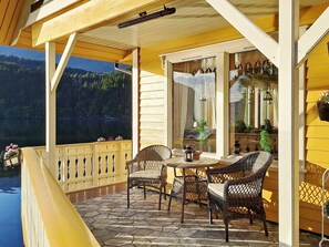 A wooden deck with wicker chairs and a table, overlooking a lake and forest. - 8 Person Holiday Home in Bygstad (Sunnfjord)