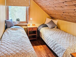 A cozy attic bedroom with two single beds, a nightstand with a lamp, and a window with a view of trees. - 8 Person Holiday Home in Bygstad (Sunnfjord)