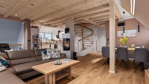 Uma sala de estar ampla com teto de madeira, um sofá, uma mesa de centro, uma escada e um espaço para refeições com cadeiras.