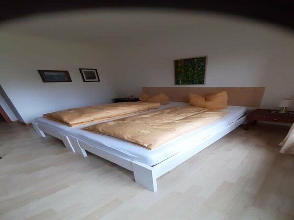 A double bed with a beige bedspread and two pillows, a nightstand with a lamp, and a painting on the wall. - House Fischergasse (Titisee-Neustadt)