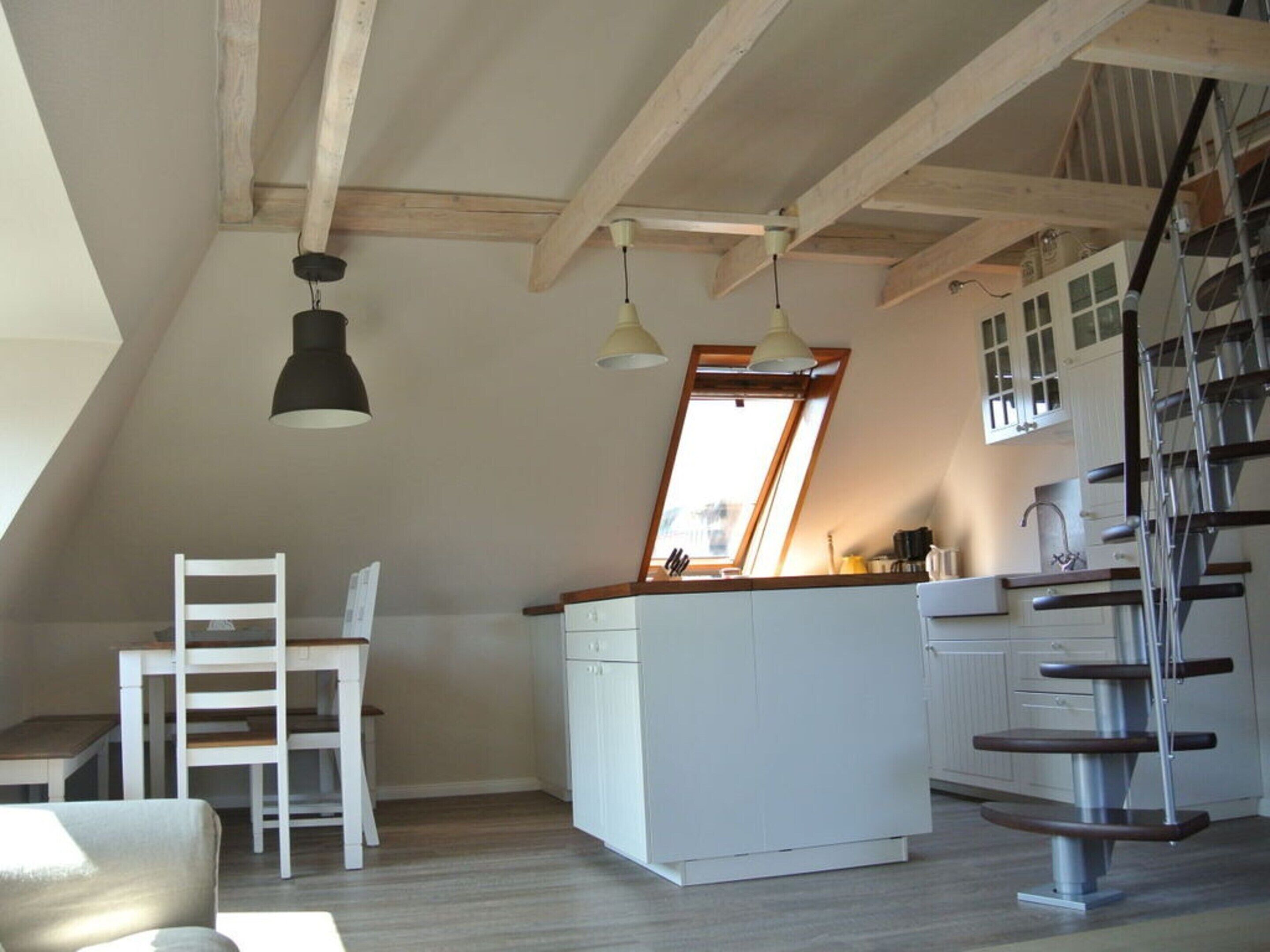 A loft-style kitchen with a wooden beam ceiling, a white island, and a dining area with a white chair.