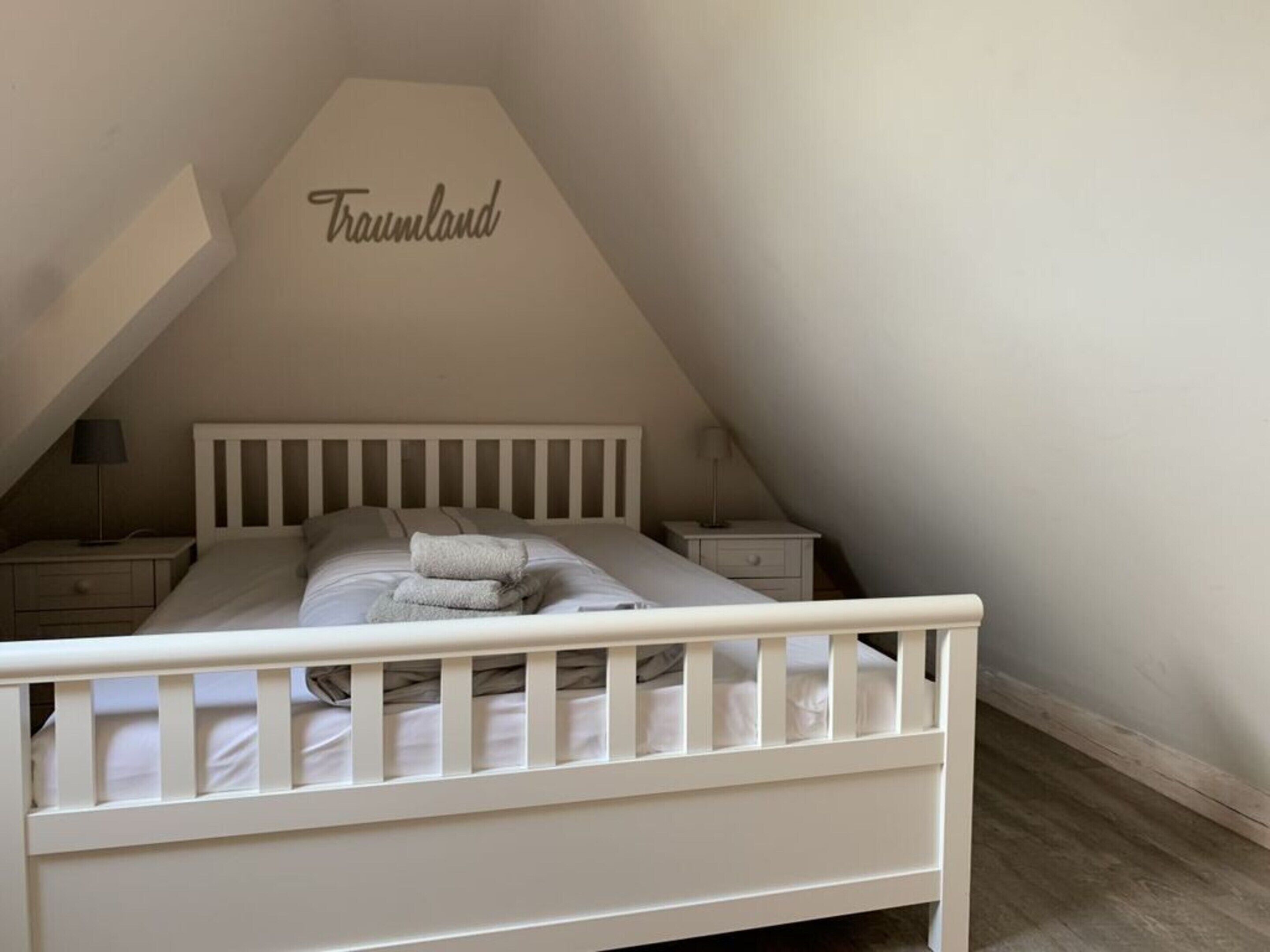 A white bed in a room with a sloped ceiling and a word 'Traumland' on the wall.
