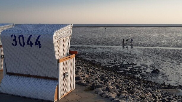 Une chaise de plage portant le numéro 3044, un rivage rocheux et quelques personnes au loin.