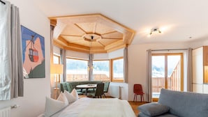 A bedroom with a bed, a sofa, a dining table with chairs, and a view of a wooden deck outside. - Apartment in Stubai Valley With Mountain View (Neustift Im Stubaital)