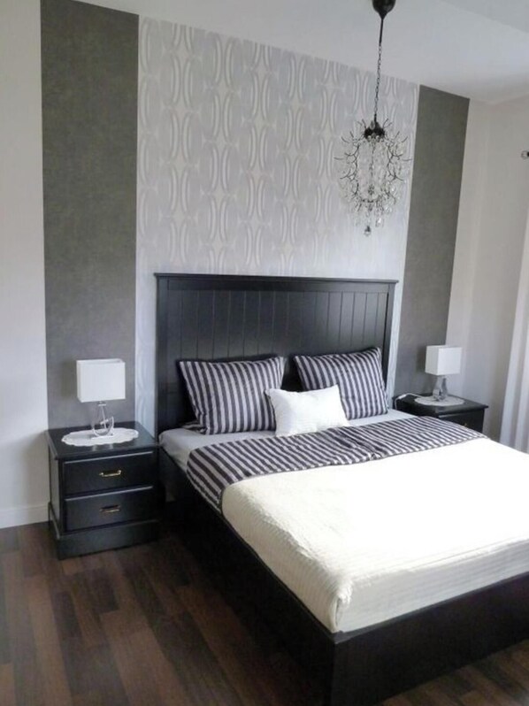 A modern bedroom with a dark wood bed, two bedside tables, a chandelier, and a patterned wall. - Holiday Apartment Schedler (Gerbrunn)