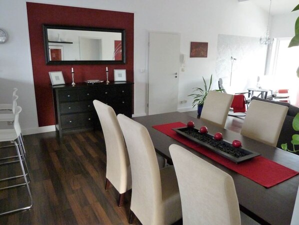 A dining area with a dark wooden table, beige chairs, a red placemat, and a decorative tray with red spherical objects. - Holiday Apartment Schedler (Gerbrunn)