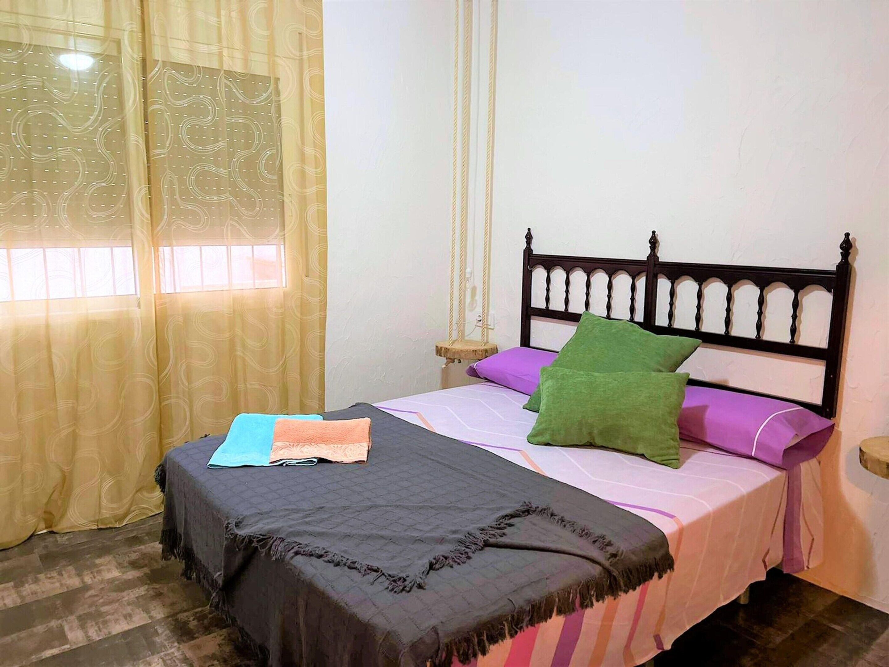 Un dormitorio con cama, mesita de noche, ventana con cortinas y cabecero de madera.
