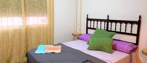 Un dormitorio con cama, mesita de noche, ventana con cortinas y cabecero de madera.