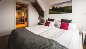 A bedroom with a large bed, a painting of a landscape, and a staircase leading to an upper level.