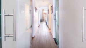 Een moderne hal met witte wanden, houten vloer en metalen deurklinken.
