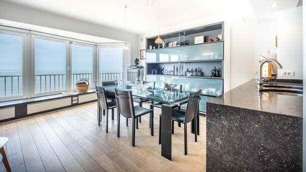 Een moderne keuken met een glazen eettafel, zwarte stoelen en een zwart granieten aanrecht.