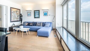 Een moderne woonkamer met een blauwe bank, een salontafel en een groot raam met uitzicht op zee.
