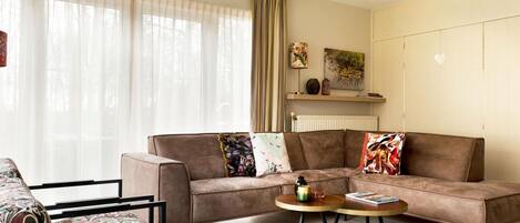 A living room with a brown sofa, a patterned armchair, a round coffee table, and a radiator.