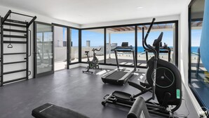 A modern gym with a treadmill, elliptical, and weight bench, featuring large windows and a view of the sea. - Penthouse Diamond | Private pool - Sea Views (Fuengirola)