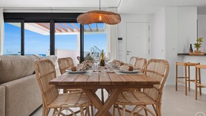 A dining area with a wooden table and wicker chairs, a hanging light fixture, and a view of the sea through large windows. - Penthouse Diamond | Private pool - Sea Views (Fuengirola)