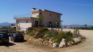 A modern two-story house with a balcony, parked cars, and a rocky garden. - Between sea and mountains (porticcio)