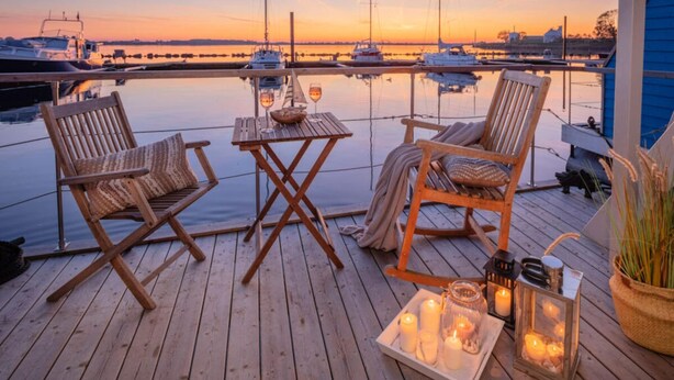En træterrasse med to fletstole og et lille bord, med udsigt over en havn med både.