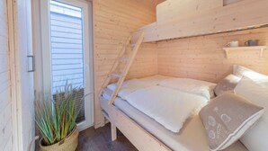 En træhytte med køjeseng, en lille hylde med kop og gryde, og en potteplante ved døren.