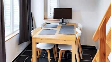 Una habitación con una mesa de madera y cuatro sillas, un televisor en un mueble bajo y una ventana con cortinas.