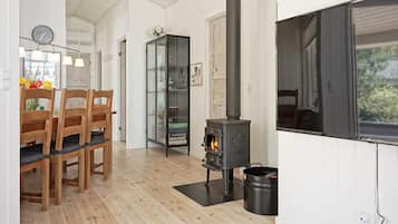 Una habitación con piso de madera, una estufa negra, un mueble vidrio y una zona de comedor con sillas de madera.