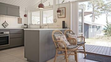 A modern kitchen with a central island, wooden chairs, and a view of the outdoors.