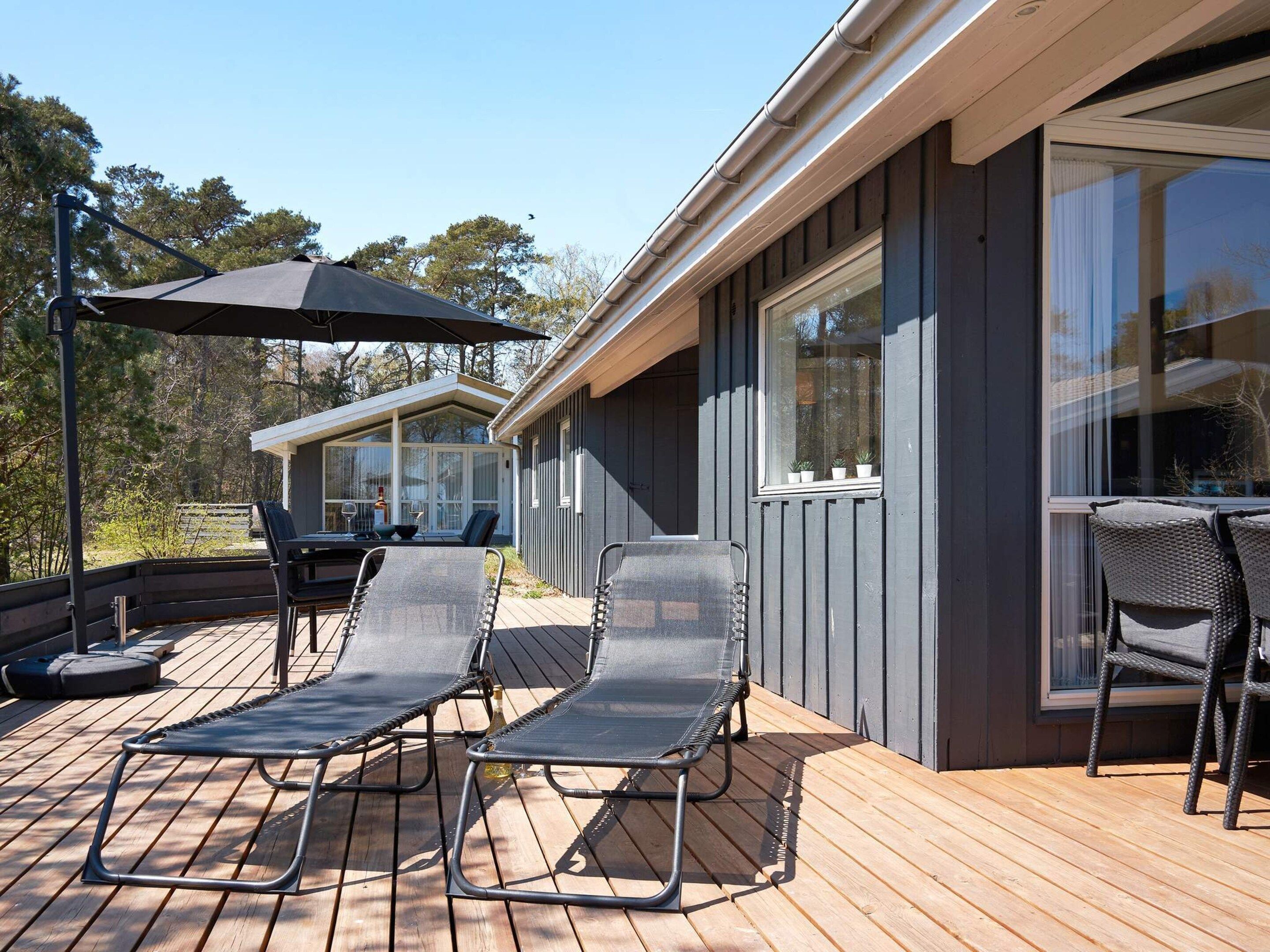 A deck with lounge chairs and a table, a covered patio area, and a building with large windows.
