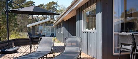 A deck with lounge chairs and a table, a covered patio area, and a building with large windows.