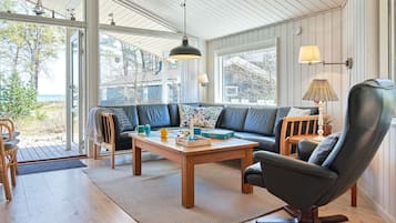 Un salón moderno con suelo de madera, un sofá de cuero, una mesa de centro y un amplio ventanal con vistas al exterior.