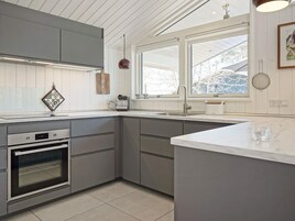 Una cucina moderna con mobili grigi, forno integrato, un'ampia finestra e un piano di lavoro in marmo.