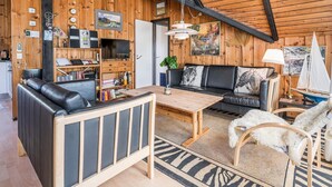 A cozy cabin interior with a wooden ceiling, a sofa, a coffee table, and a bookshelf.