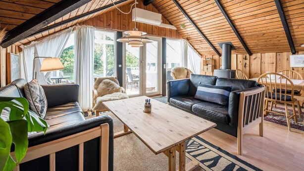 A cozy cabin interior with a wooden ceiling, a sofa, a dining table, and a fireplace.