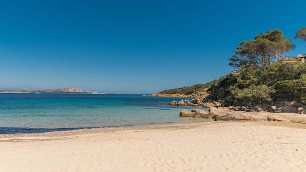 A beach with clear turquoise water, sandy shore, and rocky outcrops. - Holiday Home in Baja Sardinia With Pool (Arzachena)