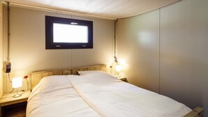 Ein Einzelbett mit Holz-Kopfteil, ein Nachttisch mit Lampe und ein Fenster über dem Bett.