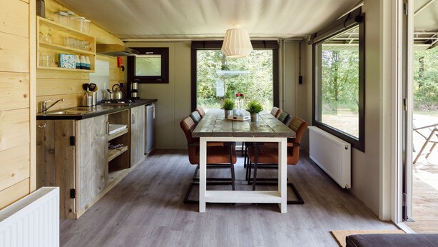Eine moderne Küche mit Holzausstattung, einem Esstisch mit Stühlen und großen Fenstern mit Blick auf Grünflächen.