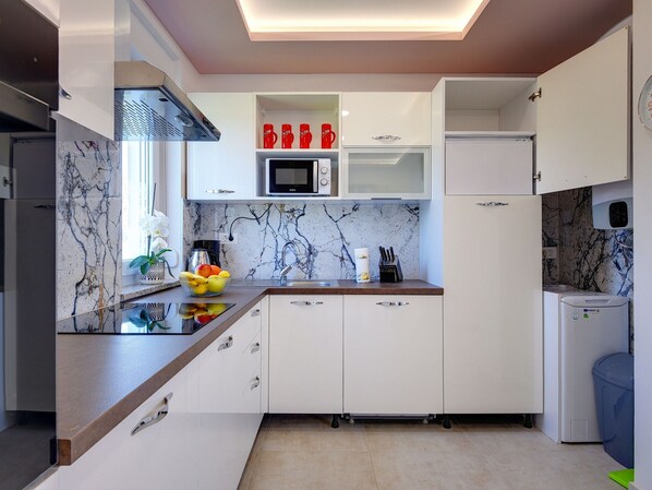A modern kitchen with white cabinets, a marble backsplash, and a built-in microwave. - Apartment in Croatia Near Stunning Coastline (Medulin)