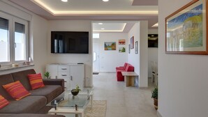 A modern living room with a sofa, coffee table, and a flat-screen TV. There is a kitchen area with cabinets and a dining table in the background. - Apartment in Croatia Near Stunning Coastline (Medulin)