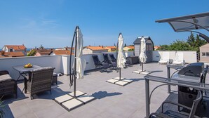 A rooftop terrace with outdoor seating, umbrellas, and a barbecue grill. - Apartment in Croatia Near Stunning Coastline (Medulin)