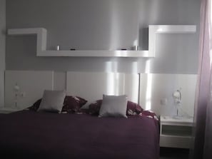 Une chambre à coucher comprenant un lit, deux tables de chevet, une commode et une étagère fixée au mur.