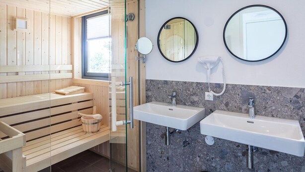 Une salle de bain moderne avec un lambris en bois, une douche à parois de verre, deux lavabos et un miroir.